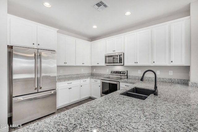kitchen featuring stainless steel appliances, a sink, white cabinets, light stone countertops, and recessed lighting