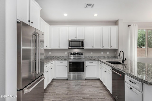 kitchen featuring appliances with stainless steel finishes, a sink, a peninsula, white cabinetry, and recessed lighting