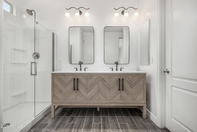 bathroom featuring wood finish floors, a shower stall, baseboards, and double vanity