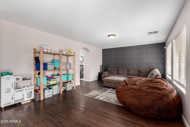 living room featuring wood finished floors, visible vents, baseboards, arched walkways, and an accent wall