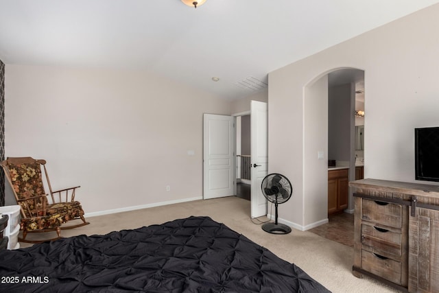 bedroom featuring light carpet, ensuite bathroom, arched walkways, baseboards, and vaulted ceiling