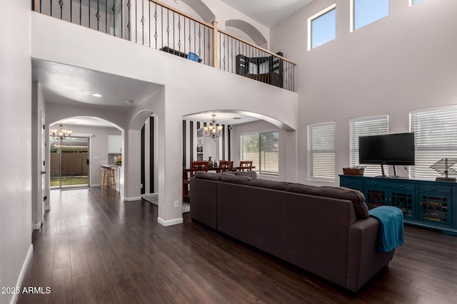 living room featuring a notable chandelier, arched walkways, dark wood-style flooring, and baseboards