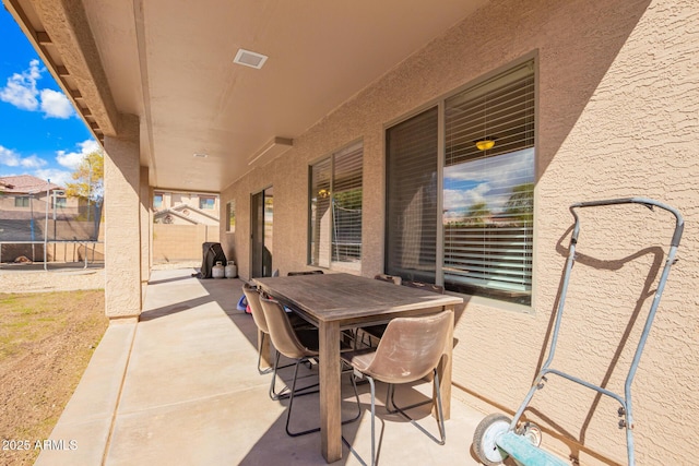 view of patio with outdoor dining area, a trampoline, and fence