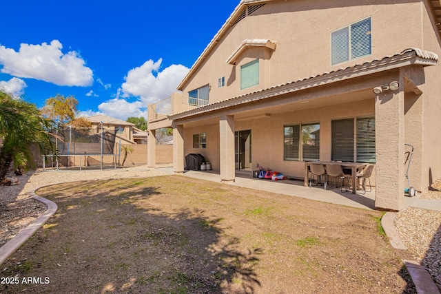 back of property featuring stucco siding, a trampoline, a fenced backyard, and a patio area