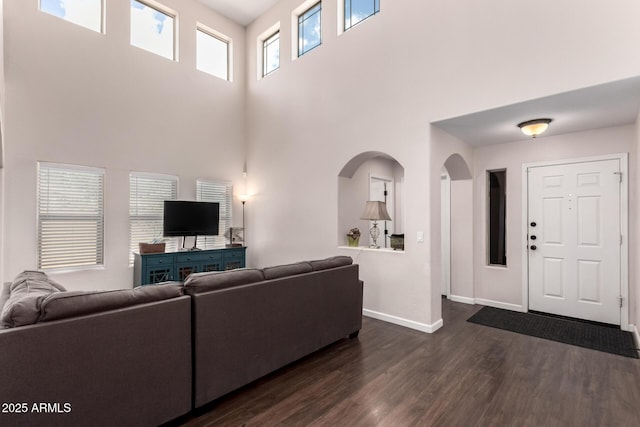 living room with a high ceiling, baseboards, dark wood-style flooring, and arched walkways