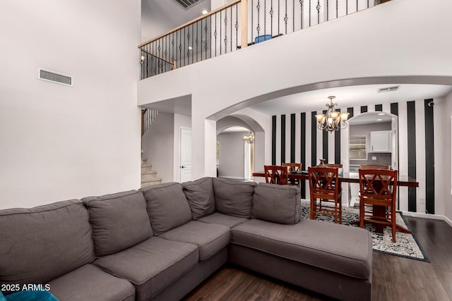 living area featuring an inviting chandelier, visible vents, arched walkways, and dark wood-type flooring
