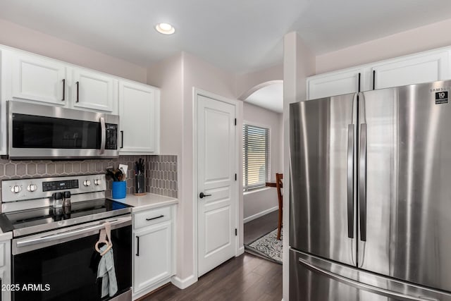 kitchen with arched walkways, white cabinets, appliances with stainless steel finishes, and tasteful backsplash