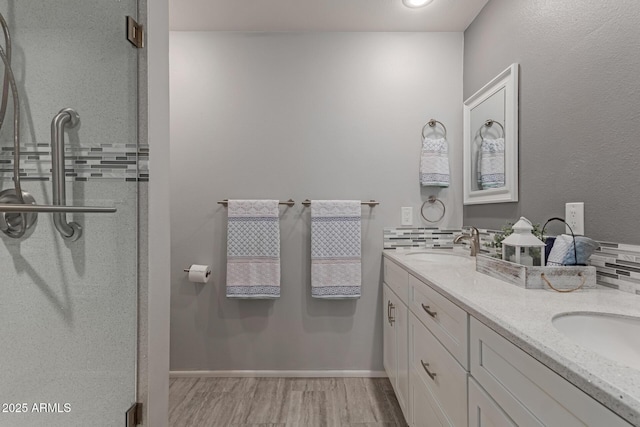 full bath with double vanity, wood finished floors, a stall shower, and a sink