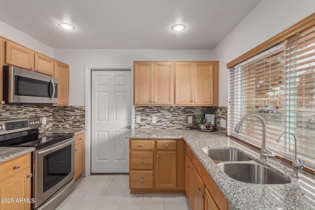 kitchen featuring a sink, decorative backsplash, light stone counters, and appliances with stainless steel finishes