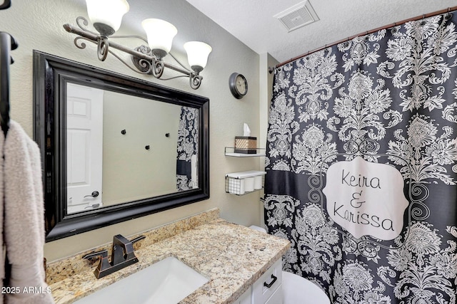 bathroom with a textured ceiling, vanity, and visible vents