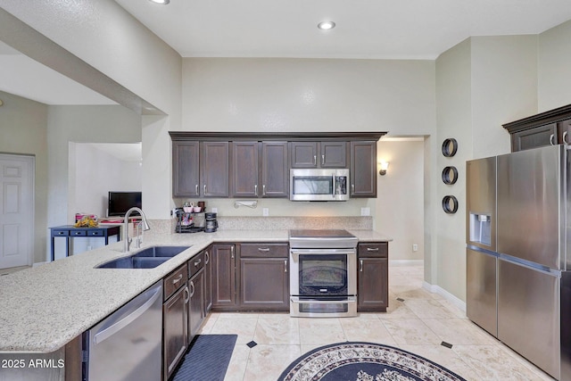 kitchen with recessed lighting, a peninsula, a sink, appliances with stainless steel finishes, and light stone countertops