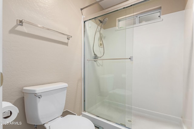 bathroom featuring a shower with door and toilet