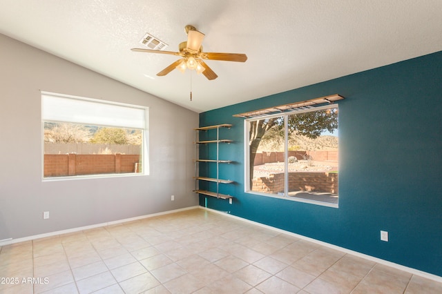 tiled empty room featuring ceiling fan, plenty of natural light, vaulted ceiling, and a textured ceiling