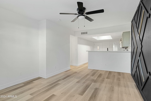 unfurnished living room with ceiling fan, light hardwood / wood-style floors, and a skylight