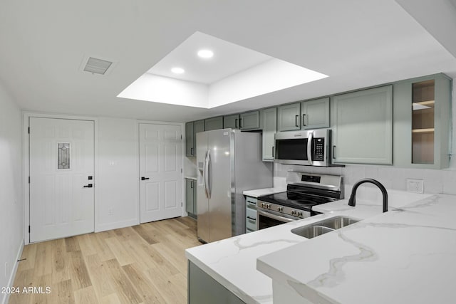 kitchen featuring sink, stainless steel appliances, light stone counters, kitchen peninsula, and light wood-type flooring