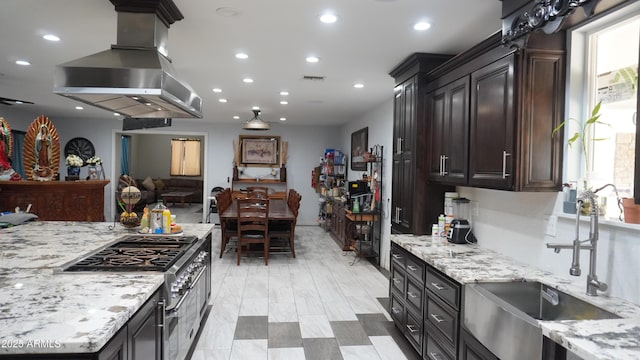 kitchen featuring high end range, visible vents, island exhaust hood, recessed lighting, and a sink