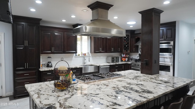 kitchen with stainless steel gas stovetop, island exhaust hood, decorative columns, a sink, and light stone counters