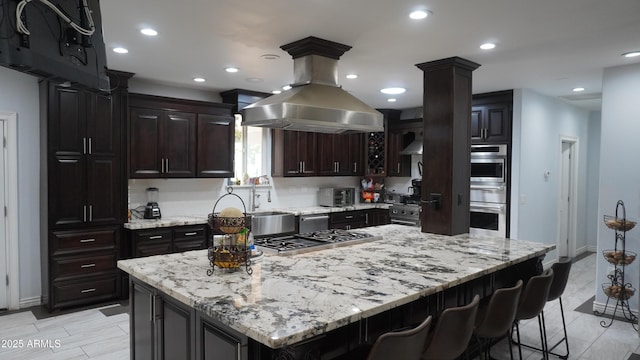 kitchen featuring island exhaust hood, a breakfast bar, stainless steel appliances, light stone counters, and a center island