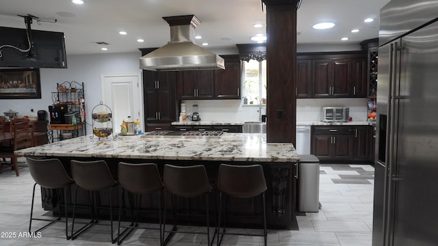 kitchen with island exhaust hood, light stone counters, a breakfast bar, and stainless steel appliances