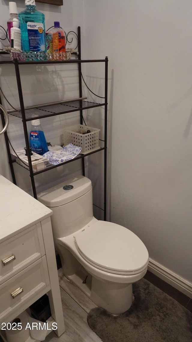 half bath featuring baseboards, toilet, vanity, and wood finished floors