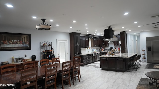 kitchen with built in refrigerator, a kitchen island with sink, recessed lighting, and light stone countertops