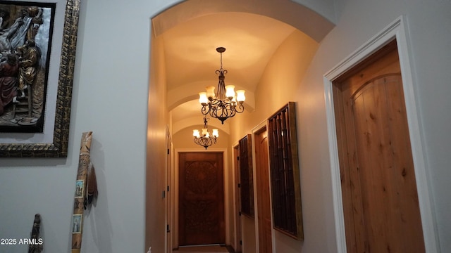 hallway with an inviting chandelier, arched walkways, and lofted ceiling