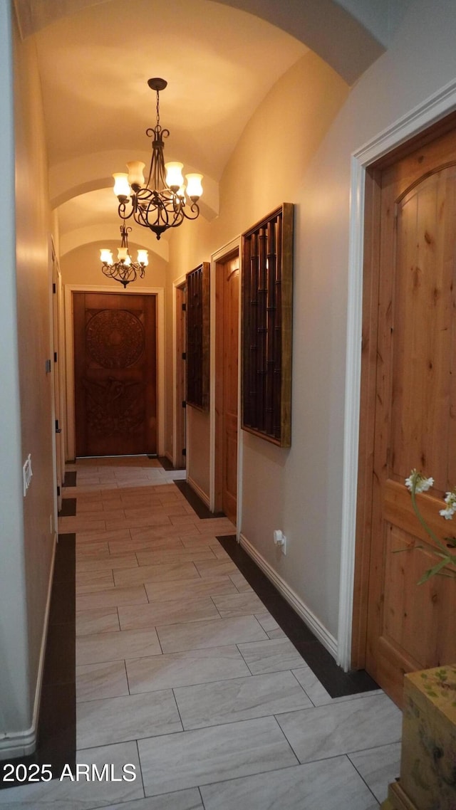hallway with vaulted ceiling, an inviting chandelier, wood finish floors, baseboards, and arched walkways