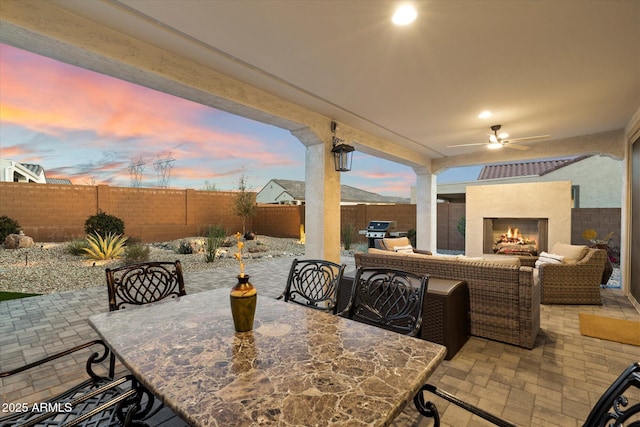 patio terrace at dusk with outdoor dining area, area for grilling, a fenced backyard, and a ceiling fan