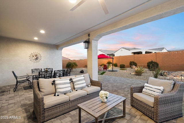 patio terrace at dusk with an outdoor hangout area, a ceiling fan, outdoor dining area, and a fenced backyard