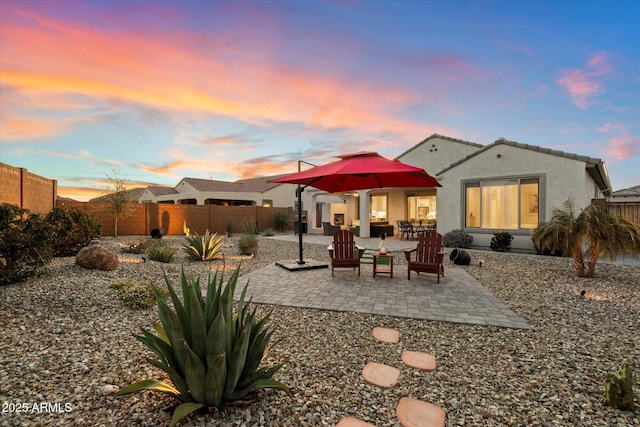 back of property at dusk featuring a patio, a fenced backyard, a tile roof, and stucco siding