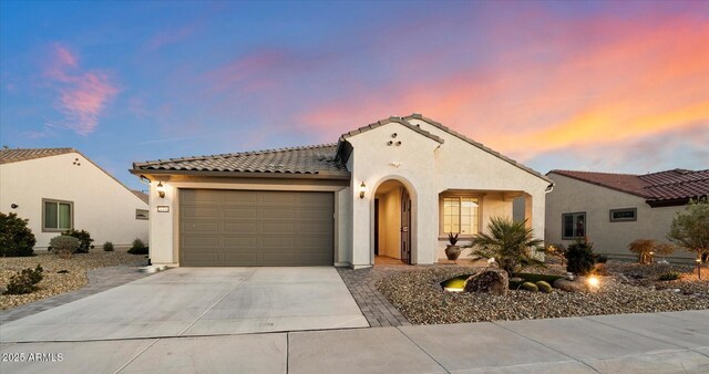 mediterranean / spanish house featuring stucco siding, a tiled roof, concrete driveway, and a garage