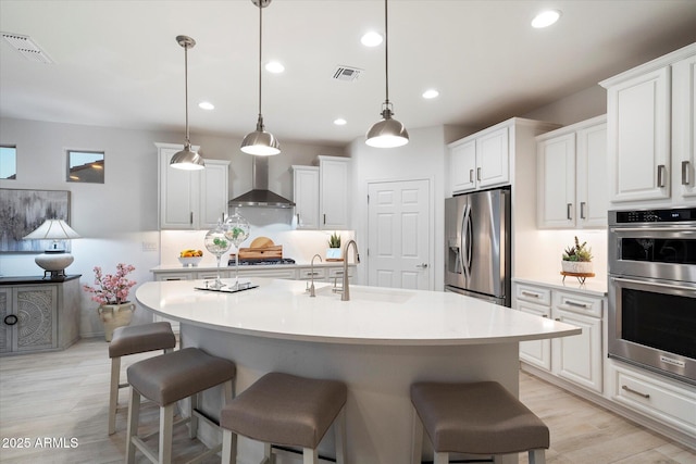 kitchen with a kitchen bar, appliances with stainless steel finishes, white cabinets, wall chimney exhaust hood, and a sink