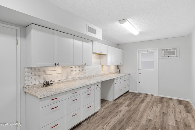 kitchen featuring a wall mounted air conditioner, light hardwood / wood-style flooring, light stone counters, and white cabinetry