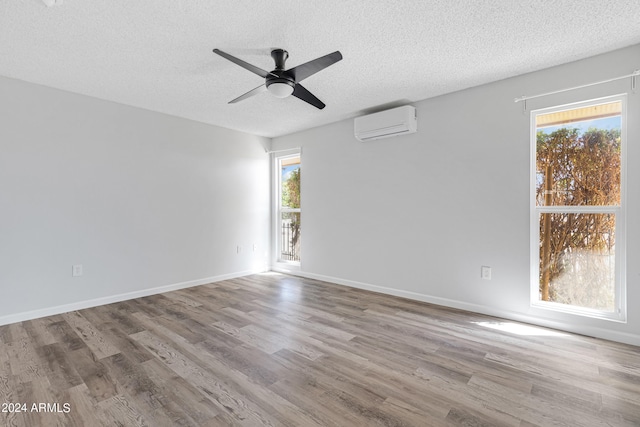 unfurnished room featuring a textured ceiling, a wall unit AC, a wealth of natural light, and light hardwood / wood-style flooring