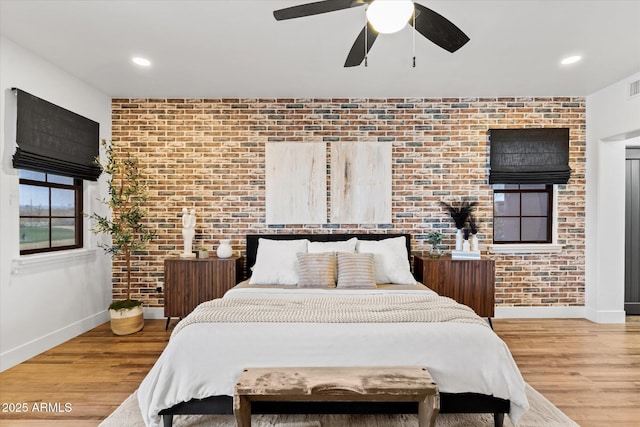 bedroom with light hardwood / wood-style floors, ceiling fan, and brick wall