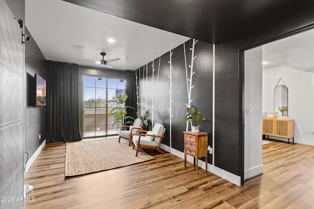 sitting room with a barn door, ceiling fan, and hardwood / wood-style floors