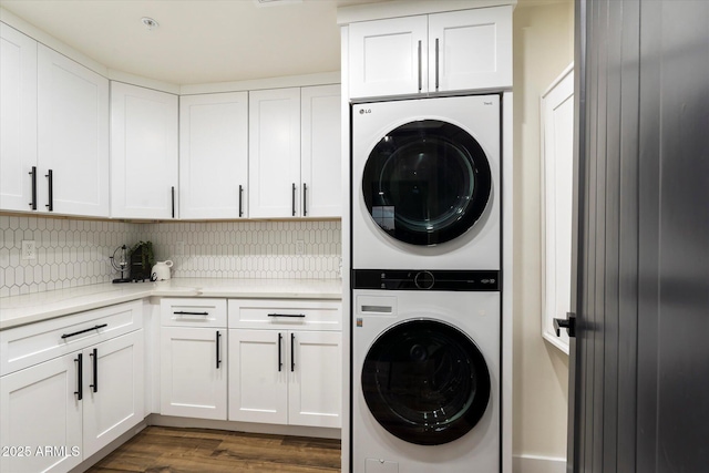 clothes washing area with cabinets, stacked washing maching and dryer, and dark wood-type flooring