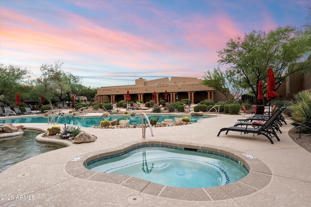 pool at dusk with a community hot tub and a patio