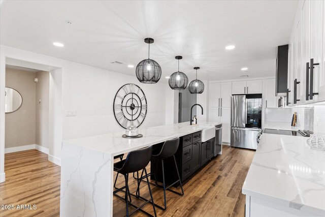 kitchen featuring hanging light fixtures, stainless steel appliances, light stone counters, a large island with sink, and white cabinets