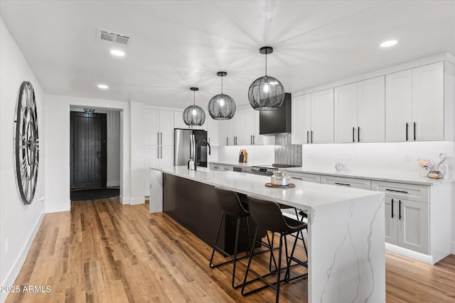 kitchen featuring a kitchen breakfast bar, pendant lighting, white cabinetry, stainless steel refrigerator, and an island with sink