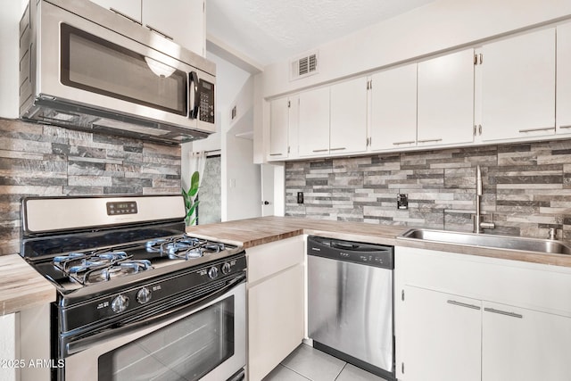 kitchen featuring visible vents, a sink, stainless steel appliances, white cabinetry, and backsplash