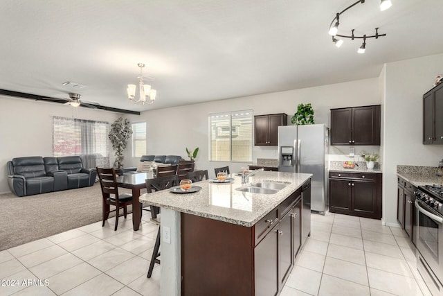 kitchen with appliances with stainless steel finishes, ceiling fan with notable chandelier, a kitchen island with sink, sink, and light tile patterned flooring