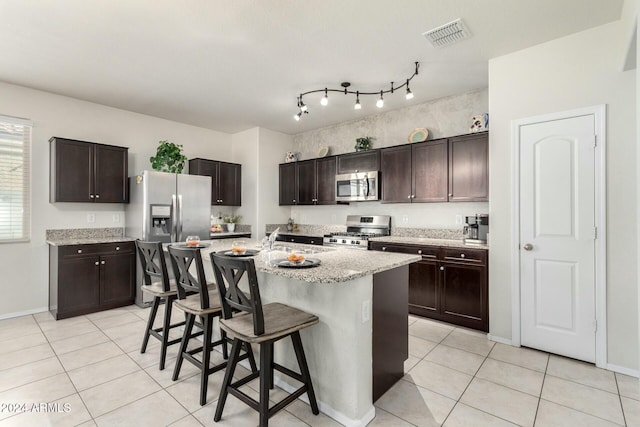 kitchen with a kitchen breakfast bar, dark brown cabinetry, a kitchen island with sink, and stainless steel appliances