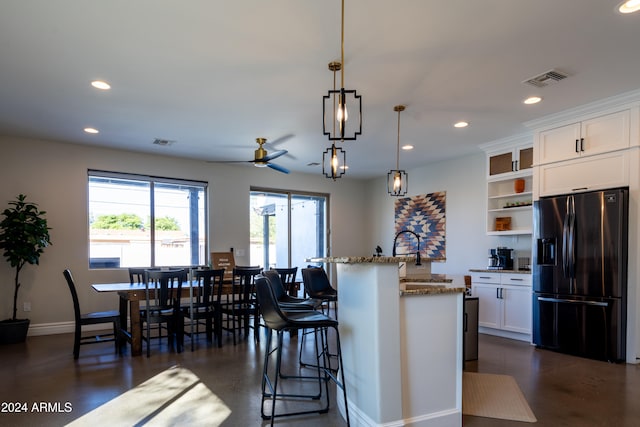 kitchen featuring light stone countertops, pendant lighting, white cabinets, stainless steel fridge with ice dispenser, and a kitchen island with sink