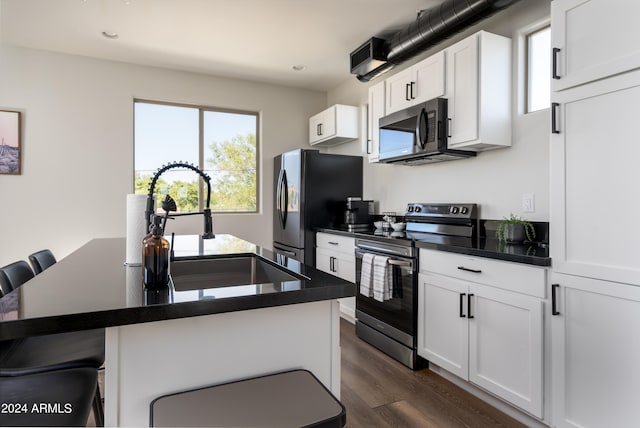 kitchen with appliances with stainless steel finishes, a kitchen bar, white cabinets, dark wood-type flooring, and a center island with sink