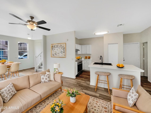 living area featuring a ceiling fan, wood finished floors, visible vents, and stairs