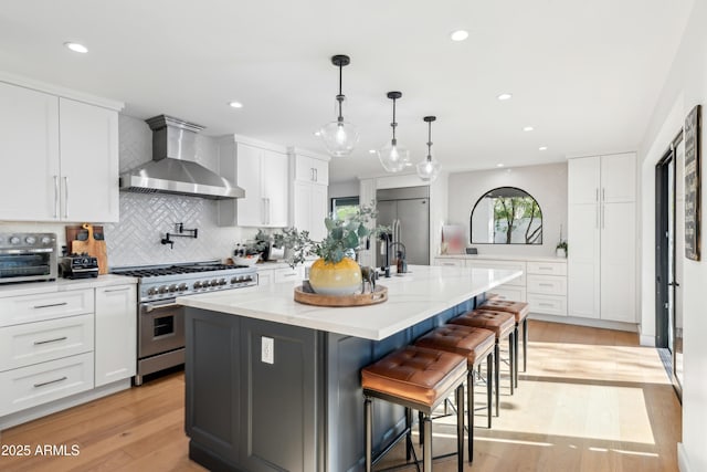 8001 N 3rd Pl, Phoenix, AZ 85020 - kitchen featuring wall chimney range hood, appliances with stainless steel finishes, tasteful backsplash, light wood finished floors, and an island with sink