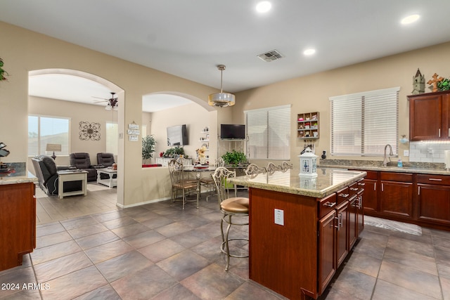 kitchen with tasteful backsplash, a kitchen breakfast bar, ceiling fan, decorative light fixtures, and a center island