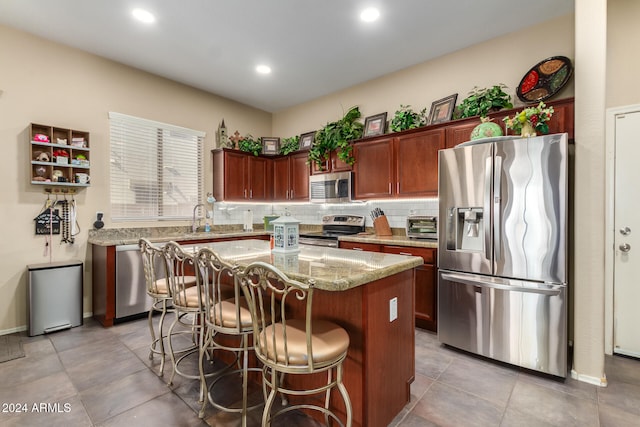 kitchen with stainless steel appliances, tasteful backsplash, a kitchen breakfast bar, light stone countertops, and a kitchen island