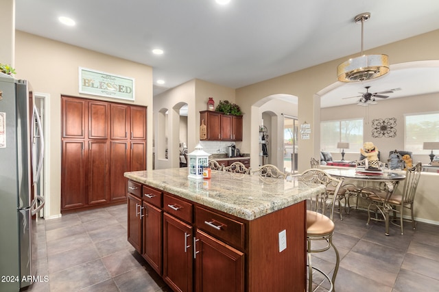 kitchen with light stone counters, a kitchen island, stainless steel refrigerator, a kitchen breakfast bar, and ceiling fan